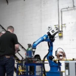 two workers drilling something with an industrial drill with a x-heat nano-heater high on the wall above them.
