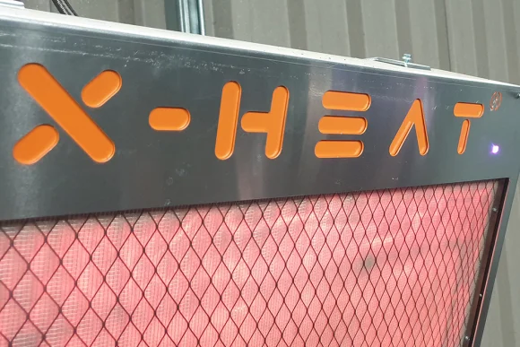 a closeup of an X-Heat Heater, it's on, the inside of it is glowing red and the logo is orange and reads 'X-HEAT'
