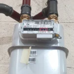 a gas meter that's attached to some pipes on a white brick wall.