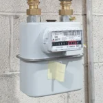 a gas meter that's attached to some pipes on a white brick wall.